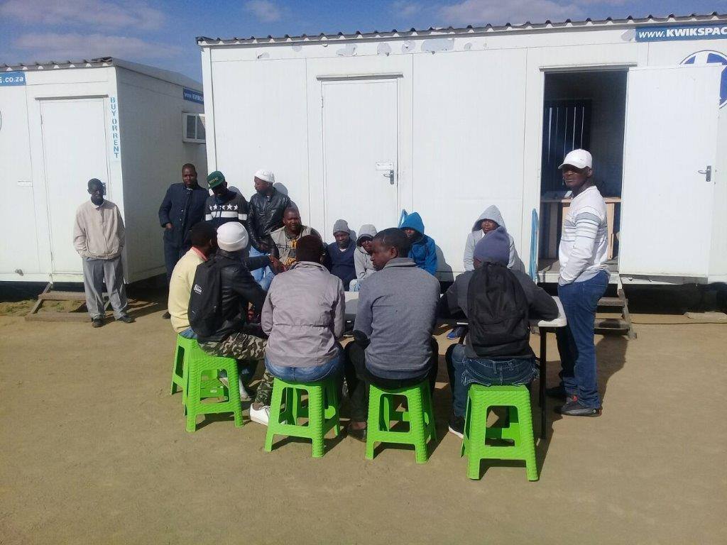 Workers gather around a table beside portable site buildings during a workplace health screening.